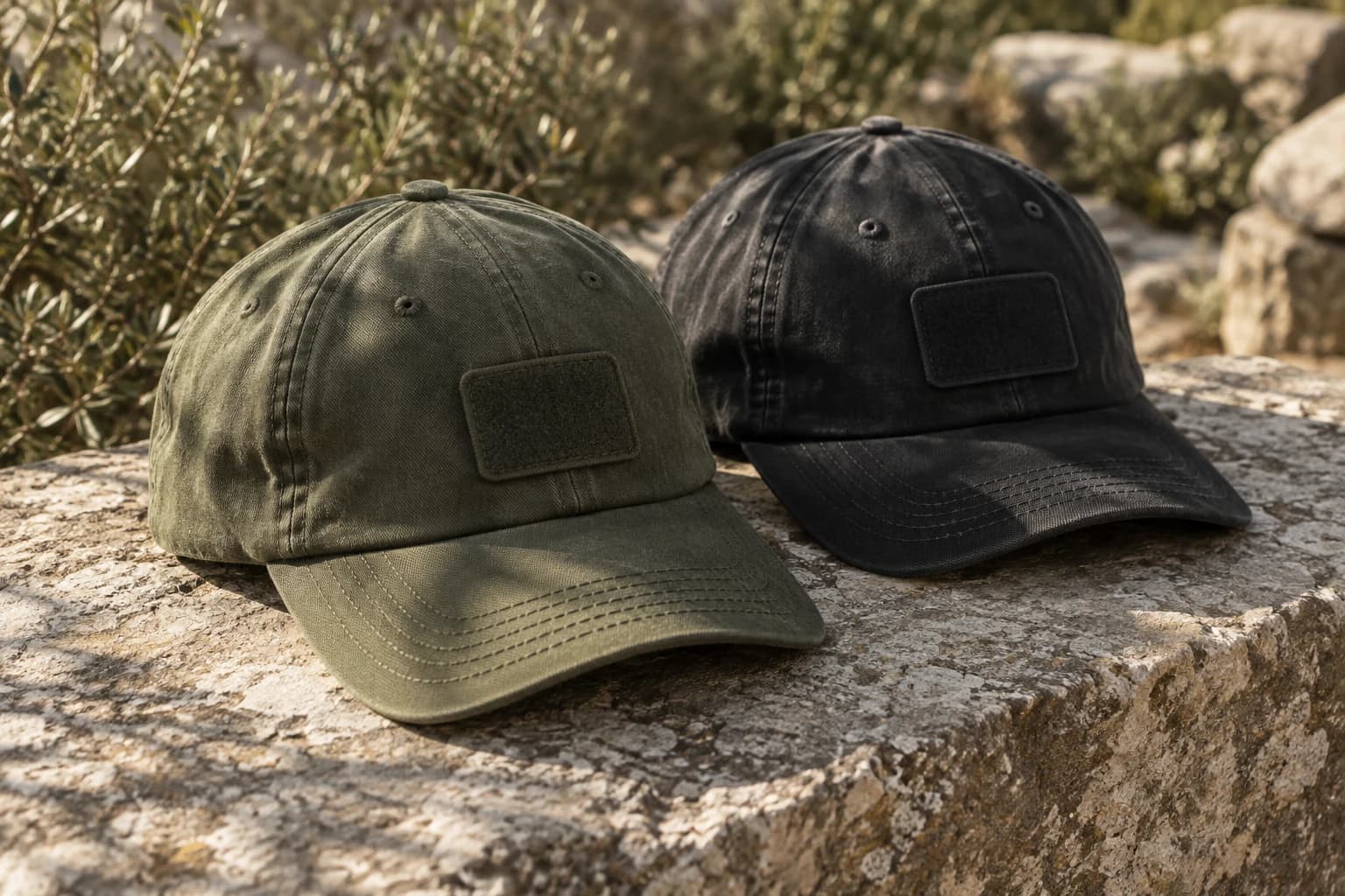 Olive and black soft-structured caps with bare tonal patch mounts, resting on sunlit stone